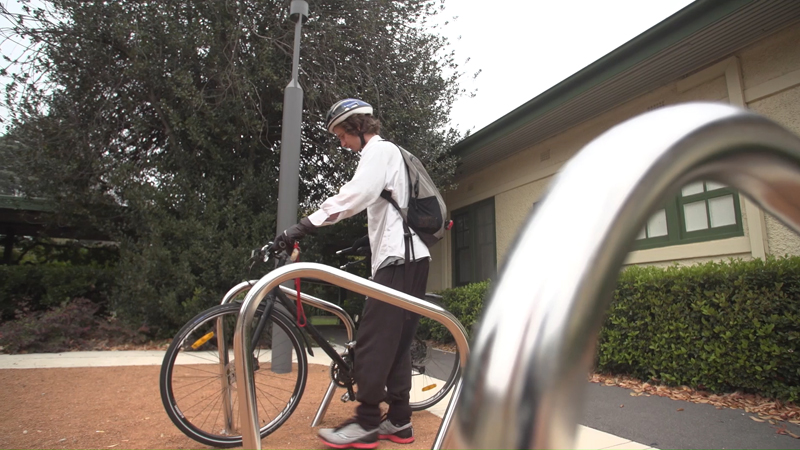 Low angle view of Stuart McMillen parking bike at bicycle racks.