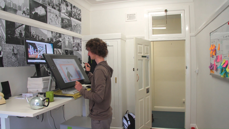 View of Stuart McMillen working at standing desk in Gorman Arts Centre art studio office.