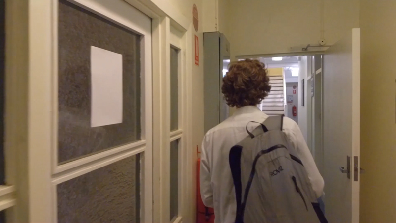 Rear view of Stuart McMillen wearing backpack walking down the hallway.