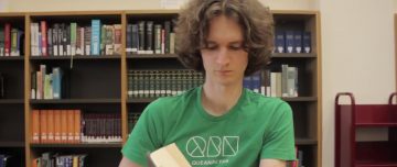 Stuart McMillen in green shirt, reading a book in the National Library of Australia