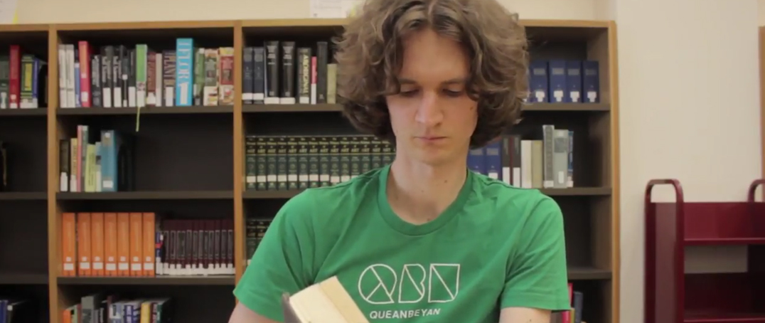 Stuart McMillen in green shirt, reading a book in the National Library of Australia