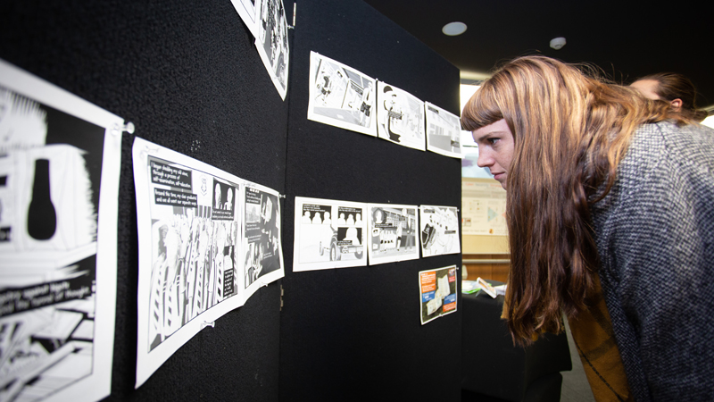 Side view of young woman looking closely at artwork on wall display