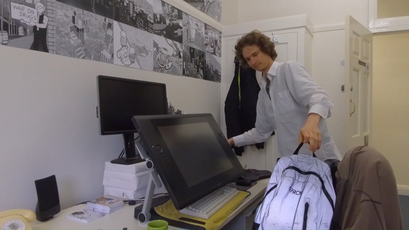 Stuart McMillen in office placing backpack on chair.