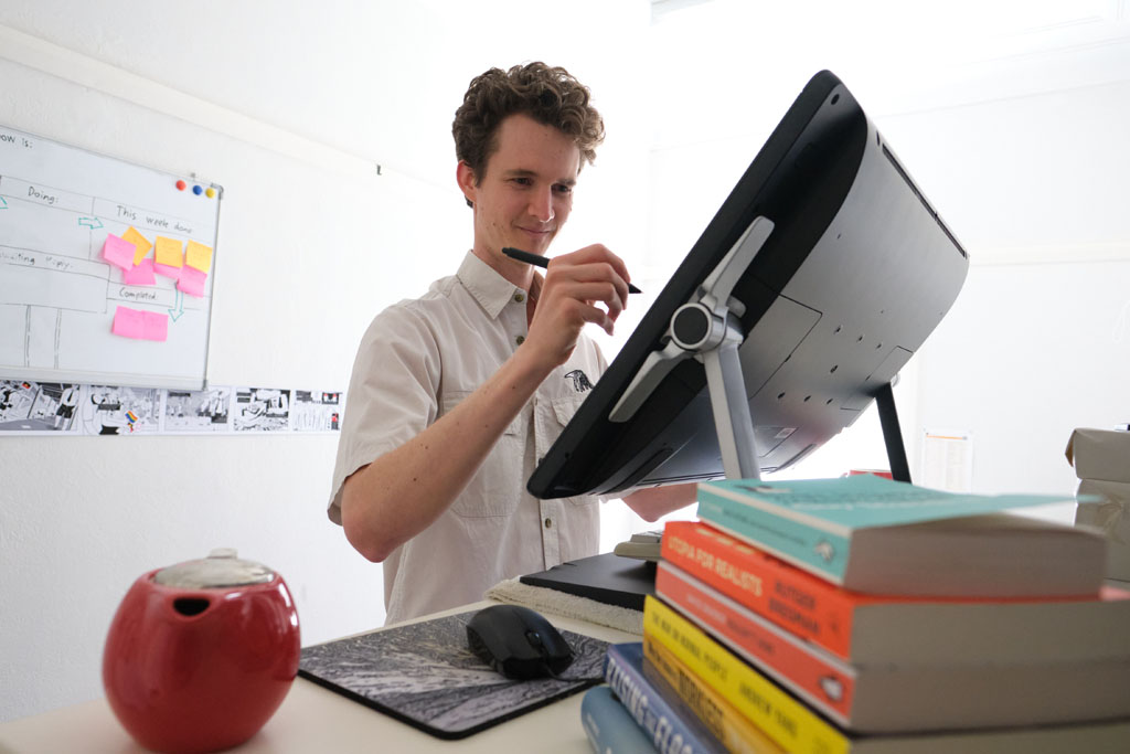 View of cartoonist using graphics tablet, shot from behind the Wacom tablet. Cartoonist Stuart McMillen in art studio