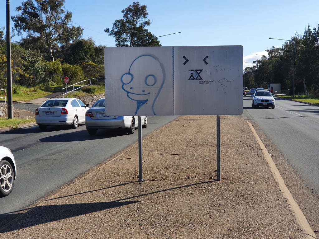 Traffic island road sign with graffiti tagged on it, in Canberra