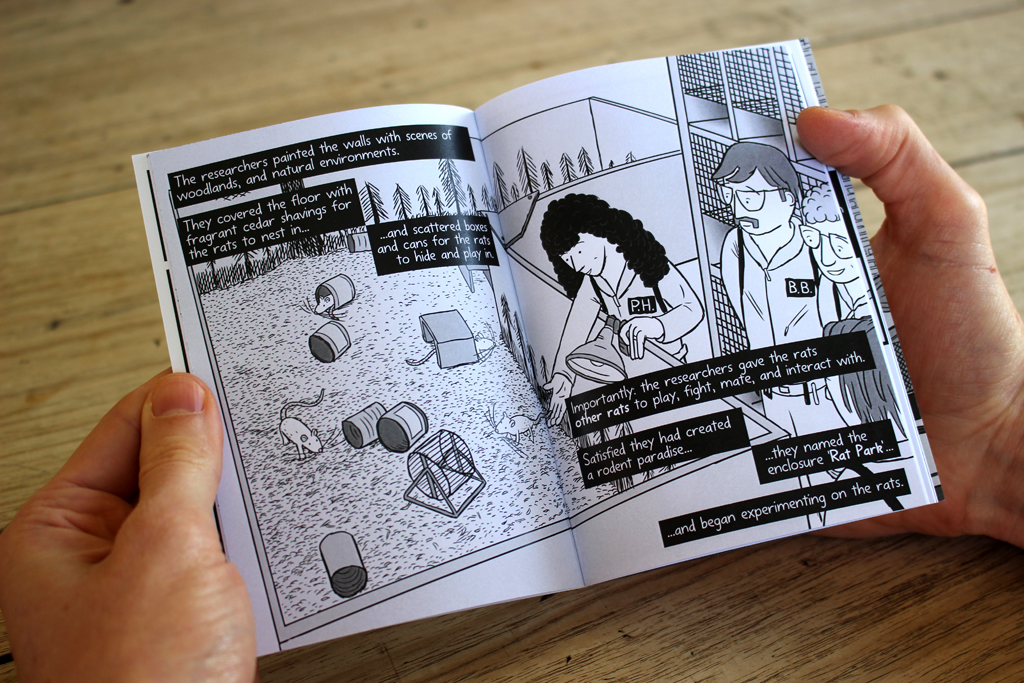 Pair of hands holding open Rat Park comic, showing a double-page spread